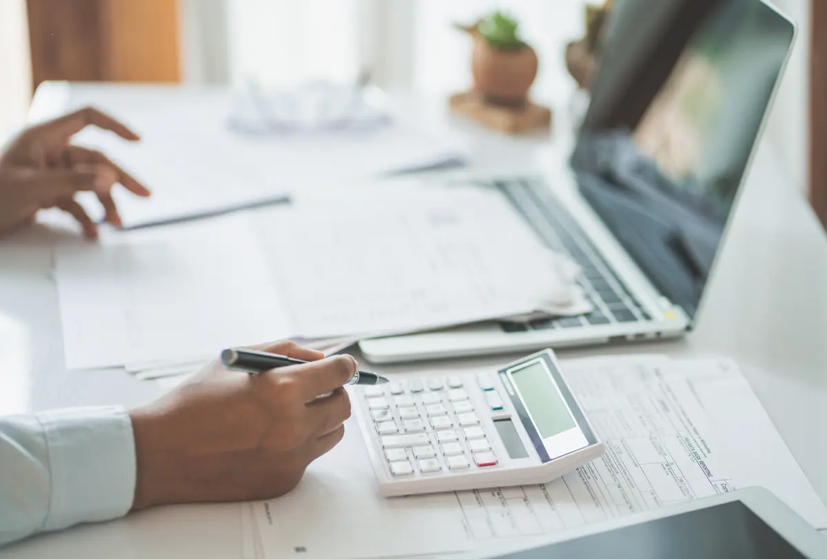 Hands working through tax papers with a calculator and laptop